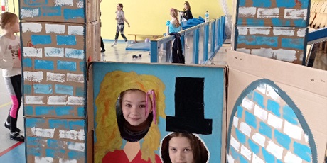 Powiększ grafikę: Dwoje dzieci pozujących do zdjęć w własnoręcznie wykonanej fotobudce “Lodowy zamek”, podczas wspólnego balu karnawałowego na sali gimnastycznej.