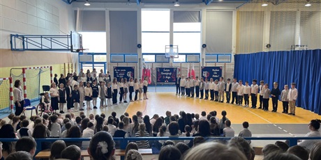 Powiększ grafikę:  Chłopcy i dziewczynki z klas 2d i 3d ustawieni w szergach odśpiewują pieśń.