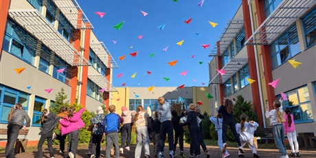 Powiększ grafikę: Uczniowie puszczaja papierowe samoloty wykonane techniką origami na dziedzińcu szkolnym.