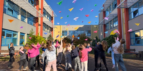 Powiększ grafikę: Uczniowie puszczaja papierowe samoloty wykonane techniką origami na dziedzińcu szkolnym.