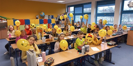 Powiększ grafikę: Uczniowie prezentują wykonane przez siebie emotki na żółtych balonach. 