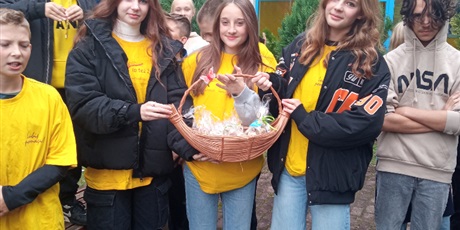 Powiększ grafikę: Uczniowie w żółtych koszulkach trzymają w rękach koszyk z cebulkami żonkili