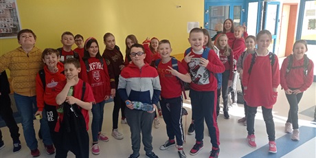 Powiększ grafikę: Grupa uczniów z klasy piątej, ubranych w czerwone ubrania, pozujących do zdjęcia na korytarzu szkolnym.