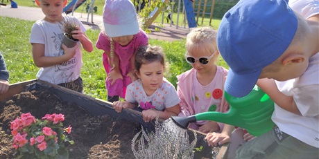 Powiększ grafikę: Dzieci sadzą i podlewają kwiaty.