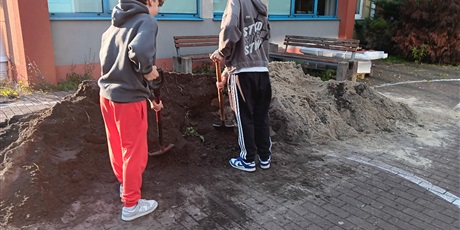 Powiększ grafikę: Uczniowie sypią ziemię łopatami.