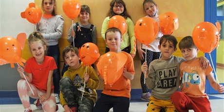 Powiększ grafikę: Uczniowie klasy 1a pozują do zdjęcia wraz z wykonanymi przez nich pomarańczowymi balonikami w kształcie słonika.