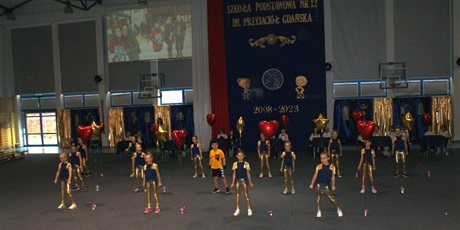 Powiększ grafikę: Występ kilkunastoosobowej grupy tanecznej z klas 2 w niebiesko-złotych strojach oraz ze złoto-czerwonymi balonami.