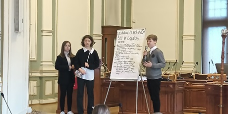 Powiększ grafikę: Uczniowie stoją na mównicy, przedstawiają swoje pomysły.