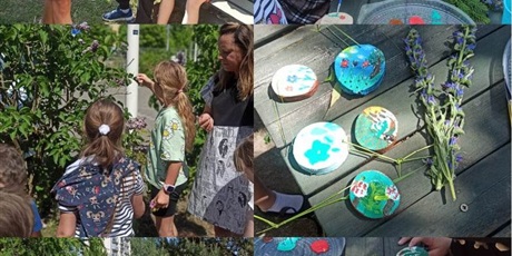Powiększ grafikę: Na zdjęciu widać Panią Marzenkę jak opowiada o roślinach. Dzieci oglądają drzewa i rośliny oraz malują farbami  na drewnianych medalionach.